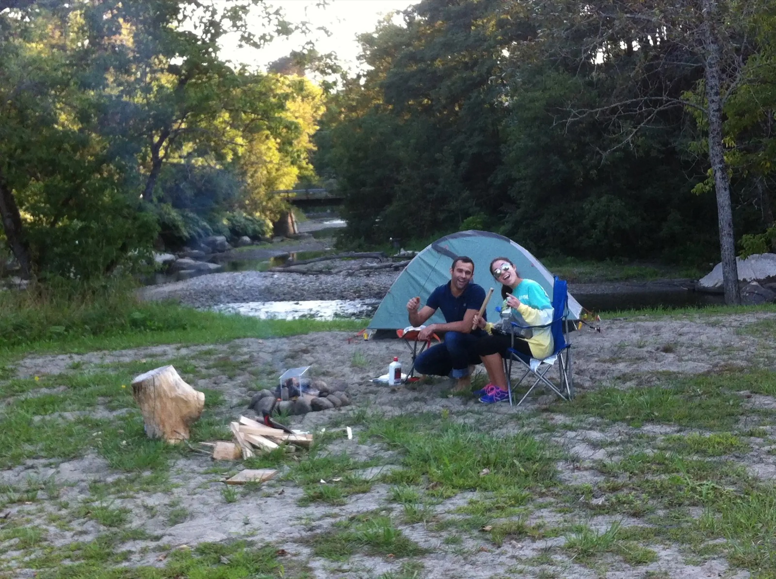 A tent site on the stony riverbank with campers and a dog